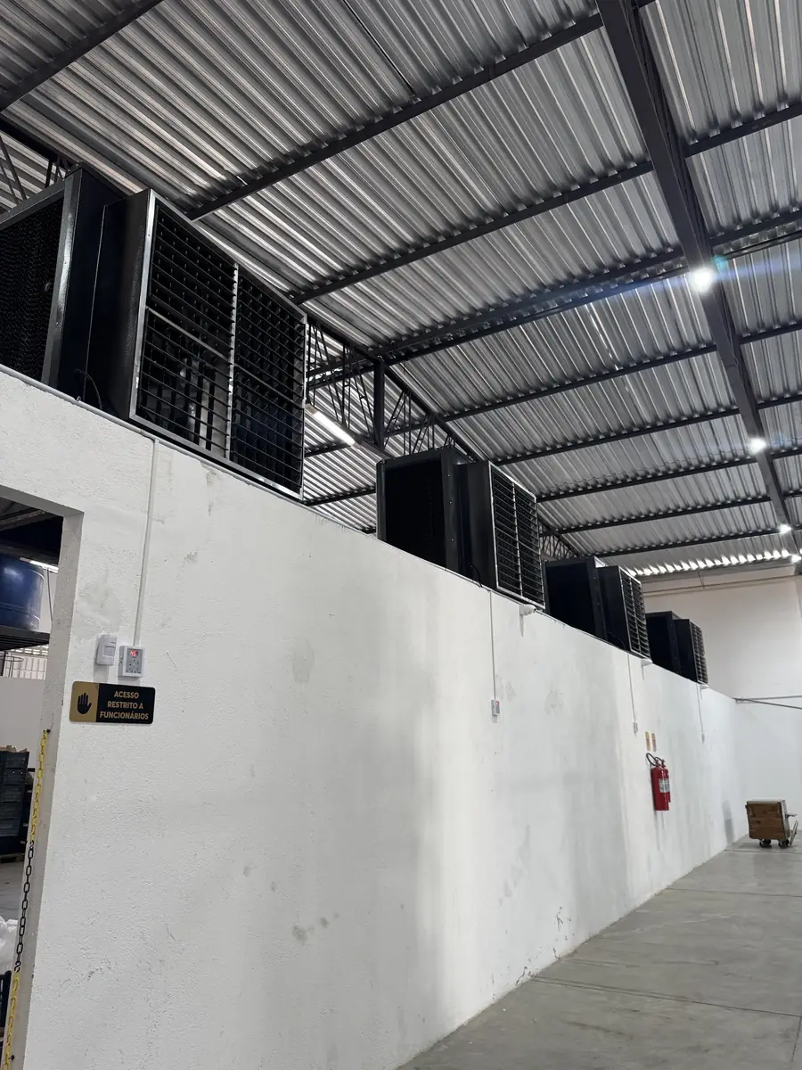 Climatizadores industriais instalados sobre a parede de um galpão com telhado metálico